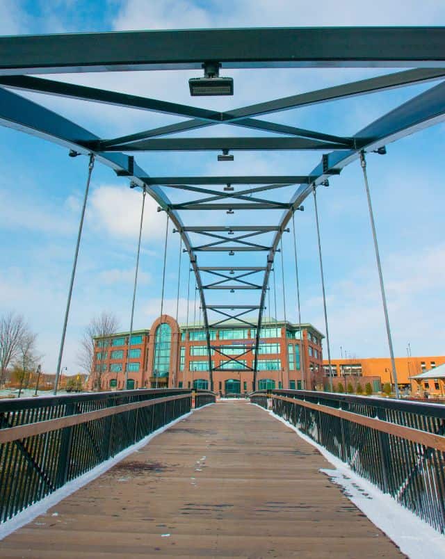 These Eau Claire, WI attractions are the best, view across a long wood and metal bridge towards a large three storey building