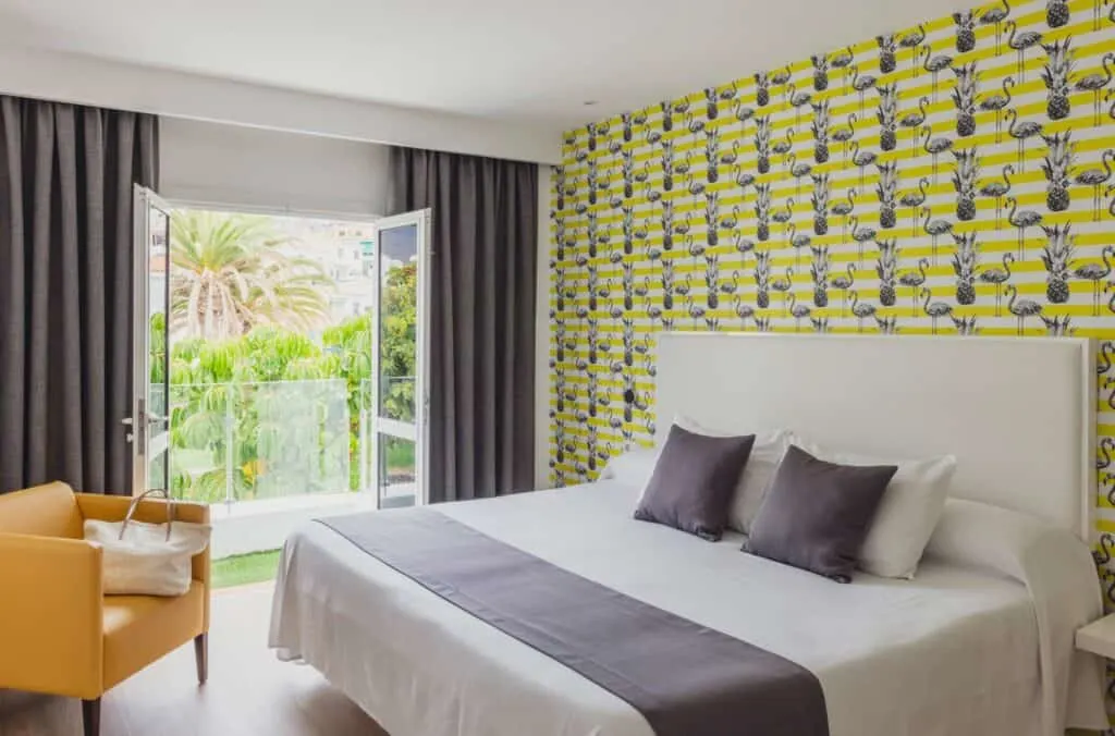 Don't miss out on the best beachfront hotels Tenerife South has to offer, hotel room interior with large bed and orange armchair next to open doors leading to balcony