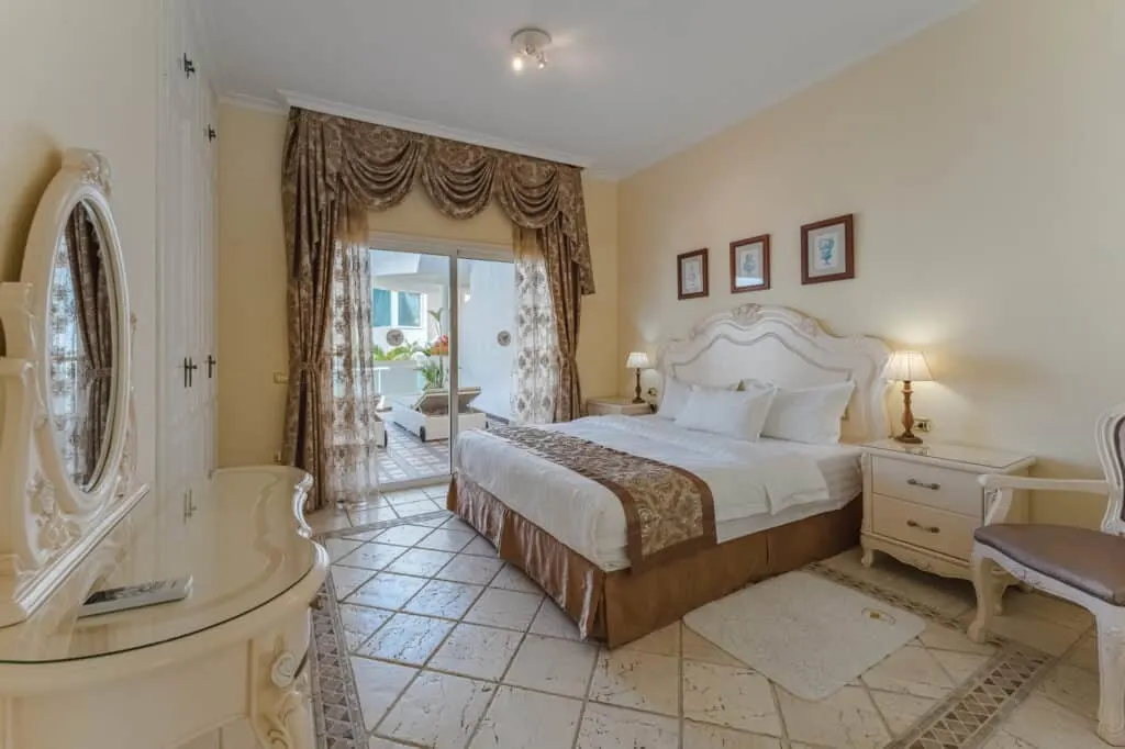 Check out some of the best beach hotels Tenerife has to offer, interior of hotel room with expensive looking decor in white and brown color scheme with vanity table and large bed and glass doors leading to large balcony area