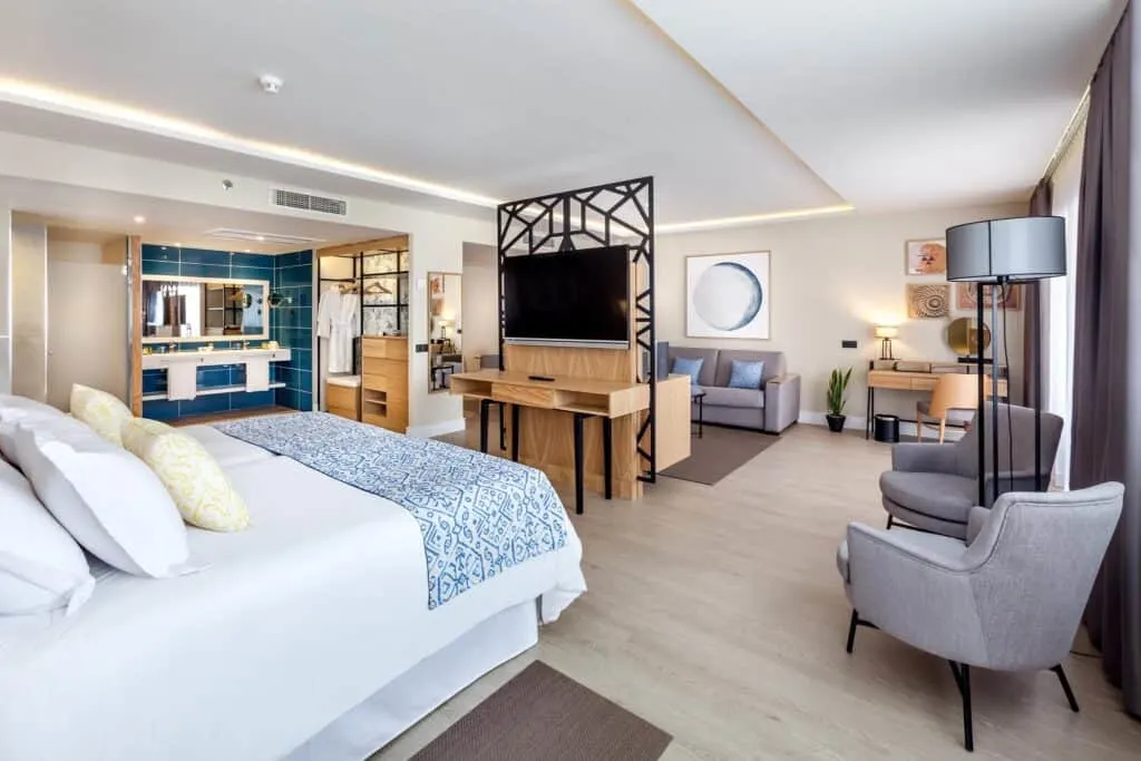 Check out these beachfront hotels in Tenerife, interior of large hotel room with grey and beige color scheme including large bed to one side and sofa and chairs along the walls 