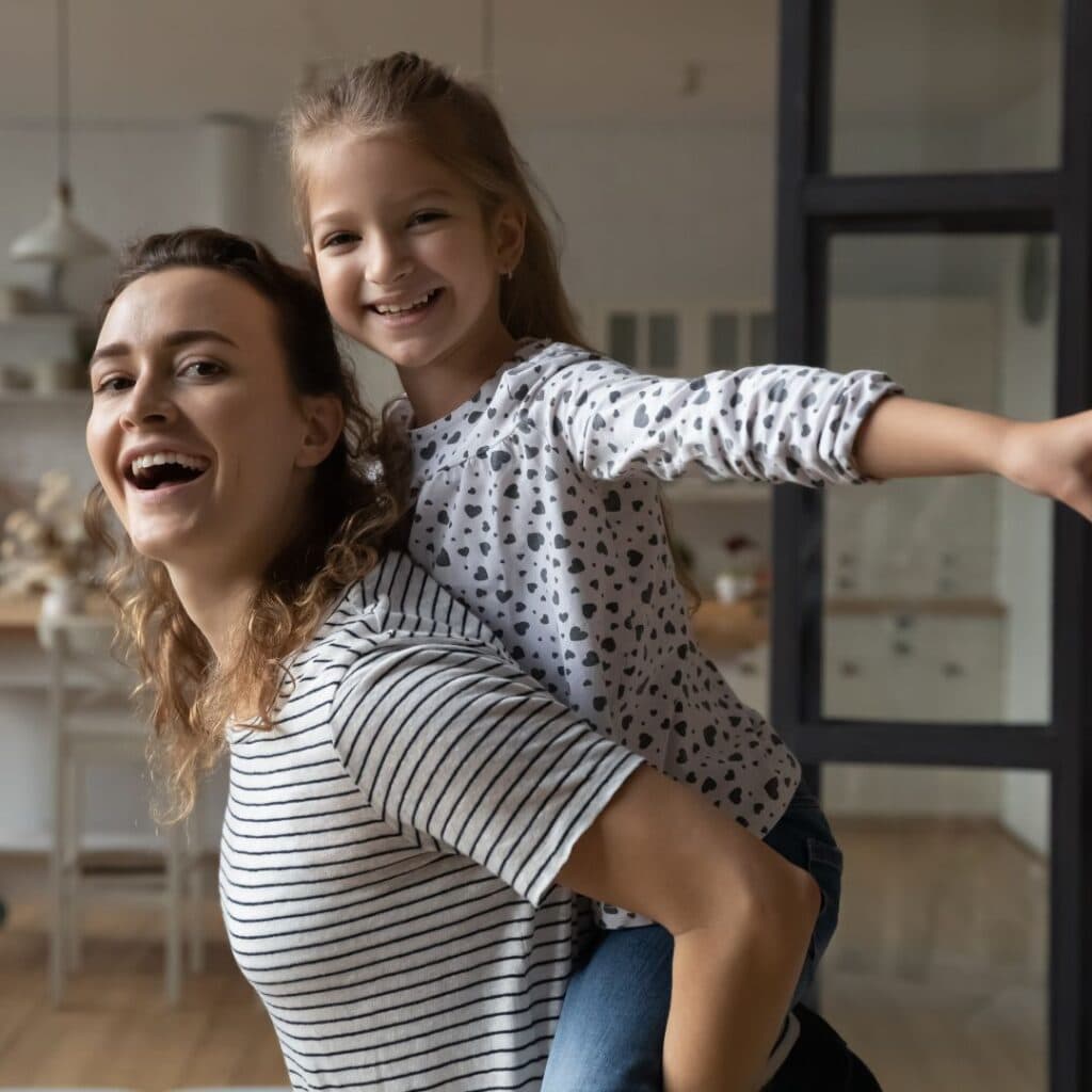 a daughter piggy back on a mom having fun in the living room