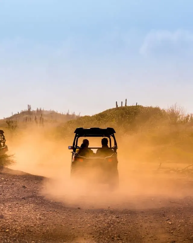 Jump into some of the best cape verde boa vista excursions, back of an off-roading vehicle with two on it driving through a dust cloud on a sandy road under a blue sky