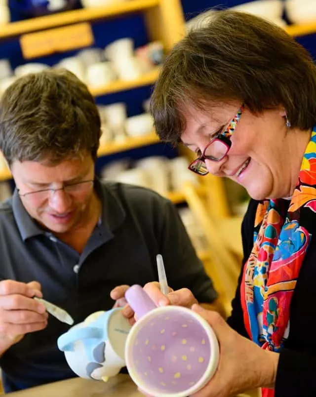 two people smiling while taking part in ceramic mug painting craft exercise