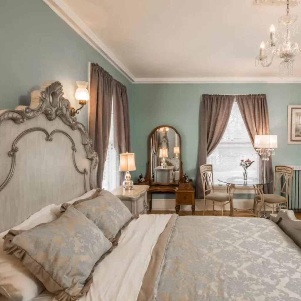 an ornate bed in a bedroom with a chandelier with light green tones and curtains by the window