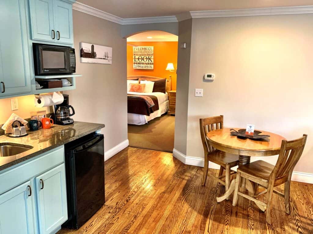 Enjoy the best adults-only hotels Wisconsin has to offer, view of kitchen area with work surface and appliances to one side and a small wooden table and chairs to the other with neatly arranged bedroom visible through a doorway in the back