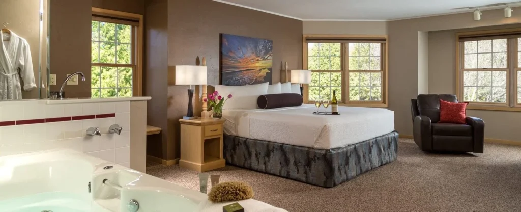 Explore Wisconsin dells for adults this summer, expansive bedroom with large bed complete with thick mattress and dark leather recliner chair with red cushion to the side and jacuzzi in the foreground