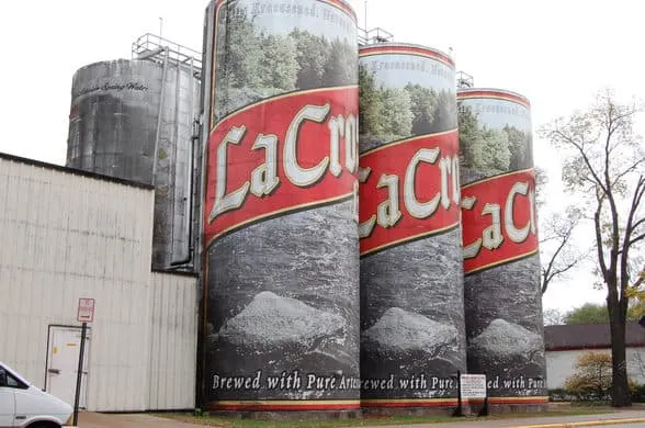 unique La Crosse attractions, tall brewery towers painted with the La Crosse logo standing next to another part of the brewery with a tree to one side and a parked vehicle to the other