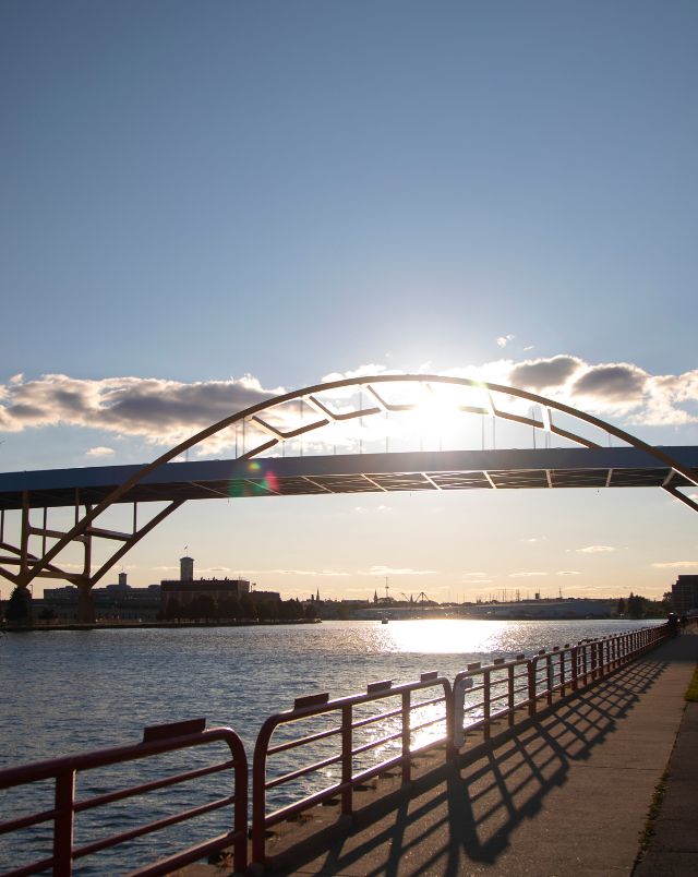 best hikes in Milwaukee, Shot of large bridge over a river with the bright sun shining behind it on a mostly clear day
