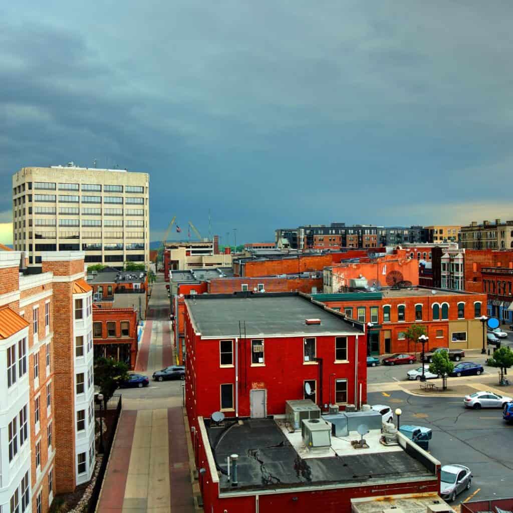 an aerial view of a city with lots of red and orange buildings and cars under a stormy sky