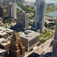 Where to go hiking in Milwaukee, Aerial view of tall skyscrapers in various shapes sitting among areas of green grass with the coast and the sea visible behind