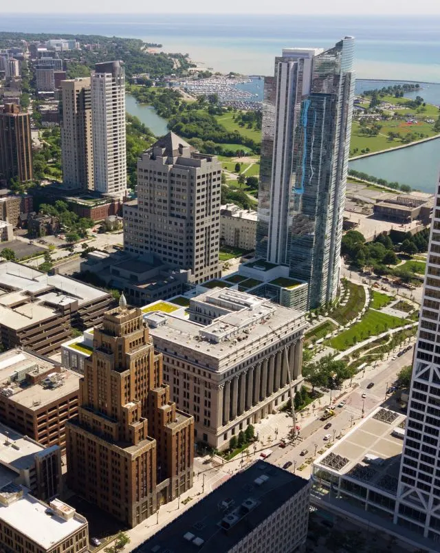 Where to go hiking in Milwaukee, Aerial view of tall skyscrapers in various shapes sitting among areas of green grass with the coast and the sea visible behind