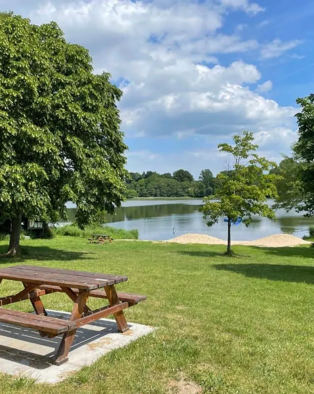 best places to visit in La Crosse Wisconsin, View of park with a picnic table and some freshly cut grass in the foreground and a large lake and green trees in the background all under a blue sky with white clouds