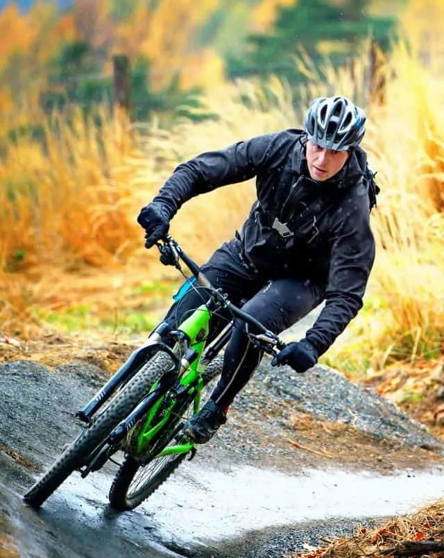 Door County March activities, Person on mountain bike with heavy outdoor clothing and cycle helmet passing around a bend on a dirt track with brown and orange shrubs behind