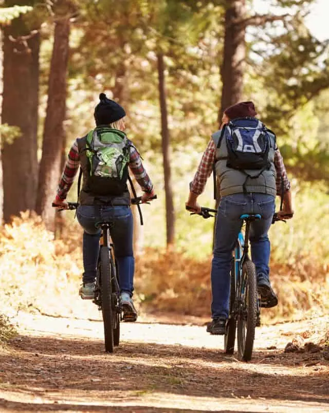 Experience the best Door County bike rides, Two people with backpacks and outdoor clothes on bikes having a conversation whilst traveling through forest on a dirt path in bright sunlight