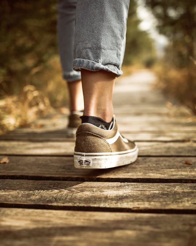 top walking trails Milwaukee offers, Close up shot of the back of someone's leg as they walk along a wooden path wearing low sneakers and three-quarter-length jeans