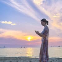 travel blogger at beach during sunset with phone