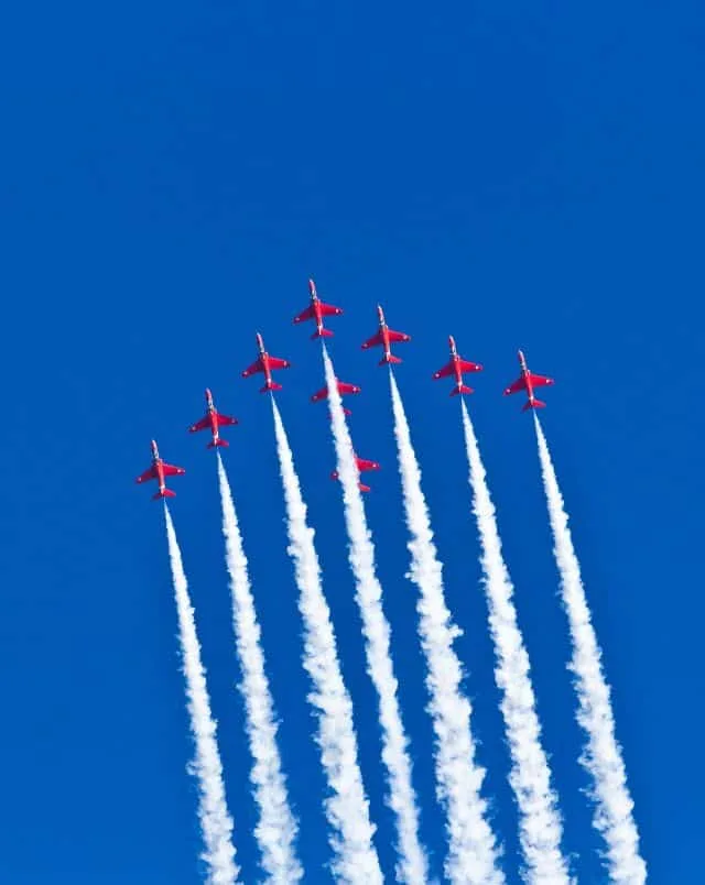 Must see events in Oshkosh Wisconsin, View of nine red airplanes flying in formation through a clear blue sky whilst spraying out white vapor behind them