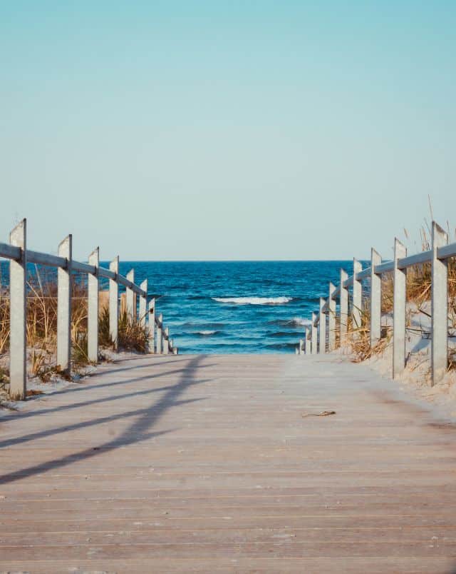 View looking across a wooden bridge towards the wide blue ocean under a clear sky