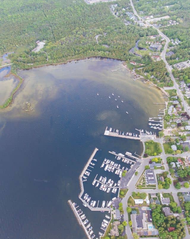 best beaches Door County offers, Aerial view of harbour with many white boats lined up in a marina built in a cove with a built up area to one side and large amounts of green trees filling in the space between the buildings