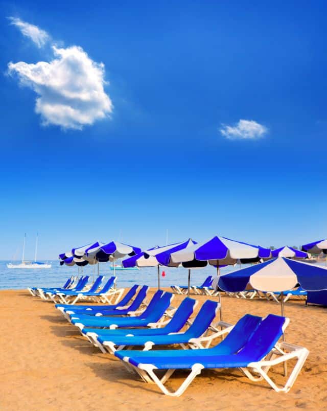 sandy beaches Tenerife South, Line of vibrant blue deck chairs with accompanying blue and white beach umbrellas all sitting on a sandy beach with the sea behind under a blue sky with a couple of white fluffy clouds