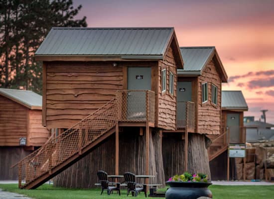 exterior of a row of log cabins on raised platforms under a sunset sky at Natura Treescape Resort, Wisconsin dells