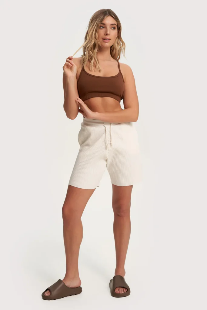 best vegan non-leather sandals, woman wearing brown sports bra, white shorts, and brown slip on sandals