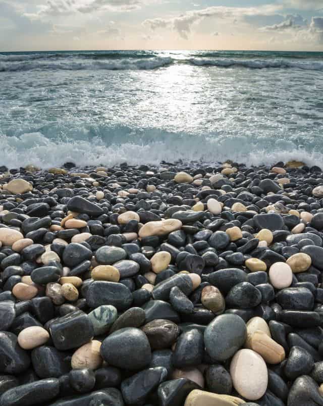 pebble beaches in Door County Wisconsin, Close up view of multicoloured pebbles and stones on the beach with foamy white surf rolling across them under a sunny sky with clouds