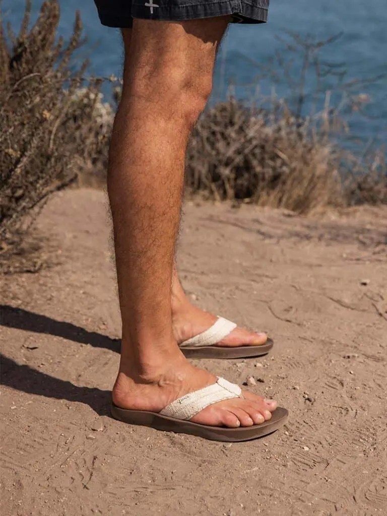 best brands for men’s vegan sandals, legs of person standing on dirt in white flip flops