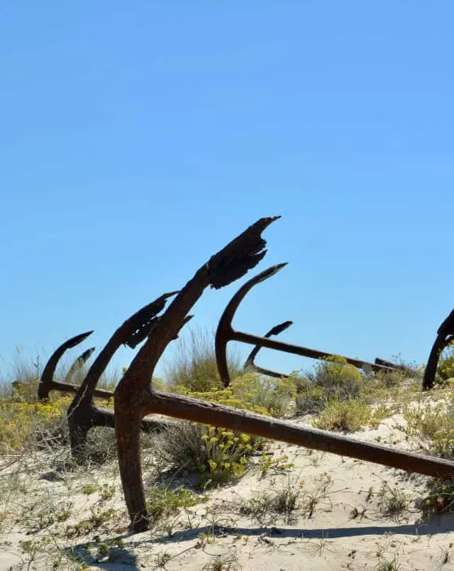 Unique Tavira attractions, Close up shot of metal anchors sitting in the sun on a sandy beach under a clear blue sky