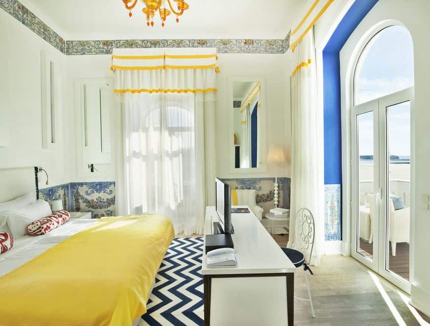 Check out these 5-star hotels in Algarve Portugal, bright and spacious hotel room with high ceilings and double bed with table and chair in front of French windows leading to balcony