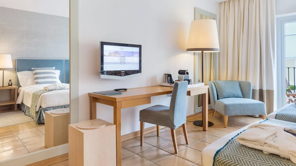 Peruse these 5-star hotels on the Algarve, hotel room with desk and chairs on one wall with large mirror reflecting a view of the large twin beds