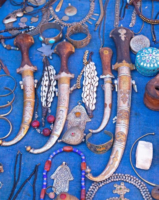 holidays to Tavira, Close up shot of a collection of ornate curved daggers and pieces of jewelry laying on a blue cloth