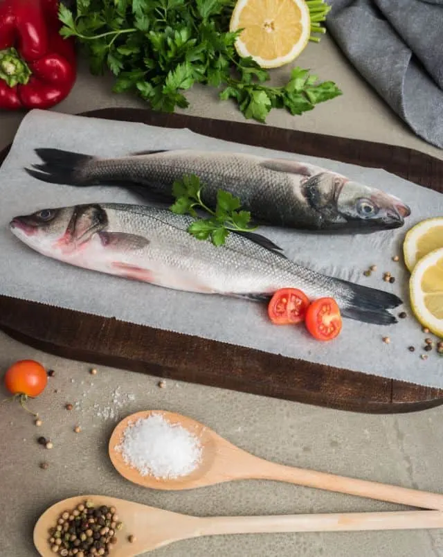 What to eat in Sagres Portugal, Overhead shot of a tray of cooked fish with lemon slices and cherry tomatoes and two wooden spoons containing portions of salt and peppercorns