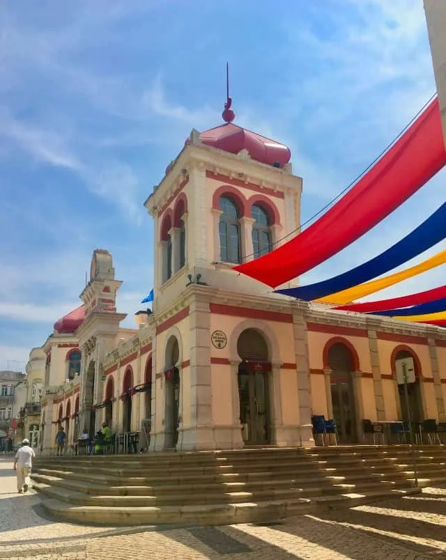 best Algarve towns, View of white stone building with red detailing and ornaments sitting atop some stone steps with colourful banners hanging across the street under a blue sky with white wispy clouds