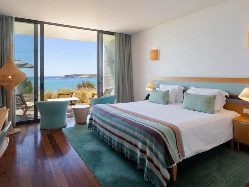 Treat yourself to the best luxury hotels in Algarve, hotel room interior with large double bed and table and chairs with large French windows leading to balcony with a view of the sea