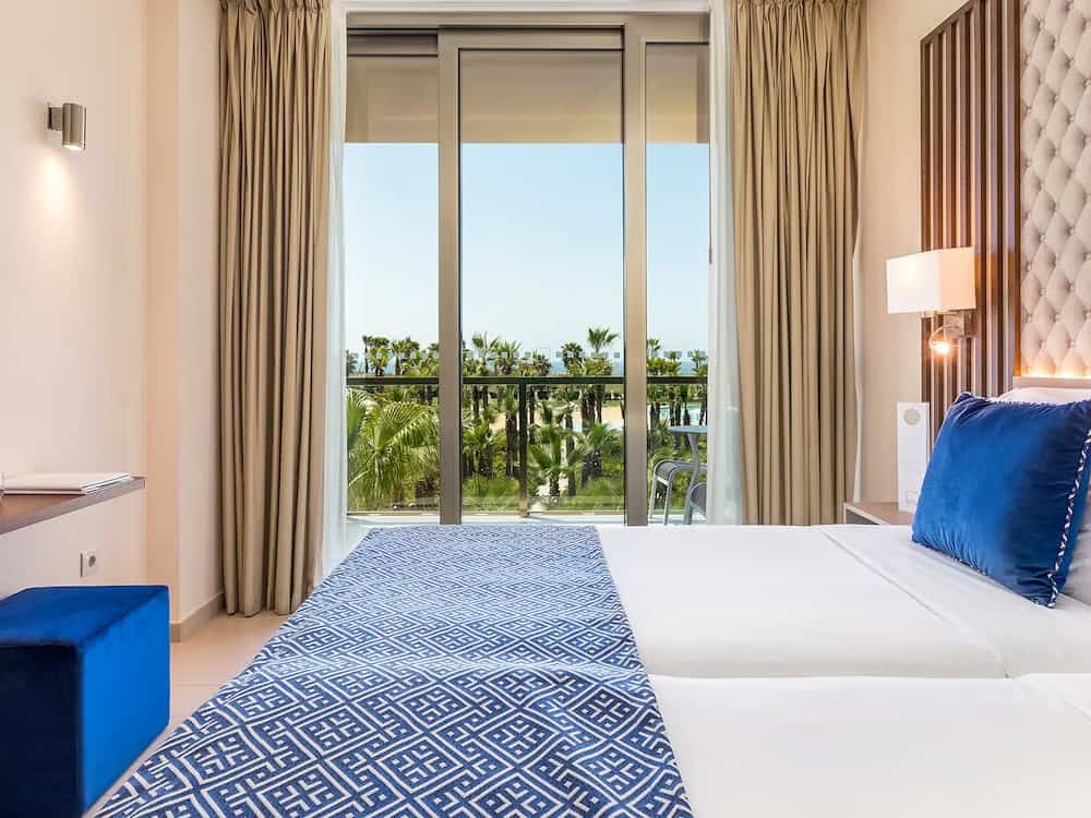 Discover the best luxury hotels in the Algarve, interior of hotel room with large double bed and high ceiling complete with sliding glass doors leading to balcony area
