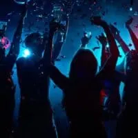 Best nightclubs in Tenerife, Wide shot of several people holding drinks in a club with low lights raising their arms as confetti falls