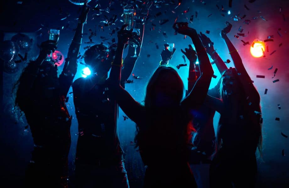 Best nightclubs in Tenerife, Wide shot of several people holding drinks in a club with low lights raising their arms as confetti falls
