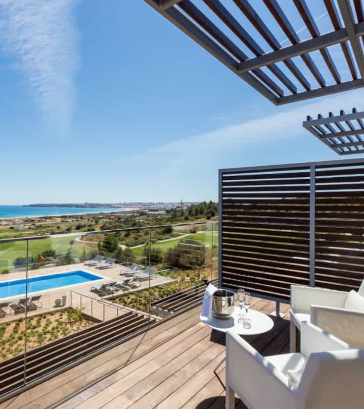 Enjoy a 5-star hotel Algarve vacation this year, hotel room balcony with table and chairs with view of pool area and wide vista of surrounding green landscape with the sea in the distance