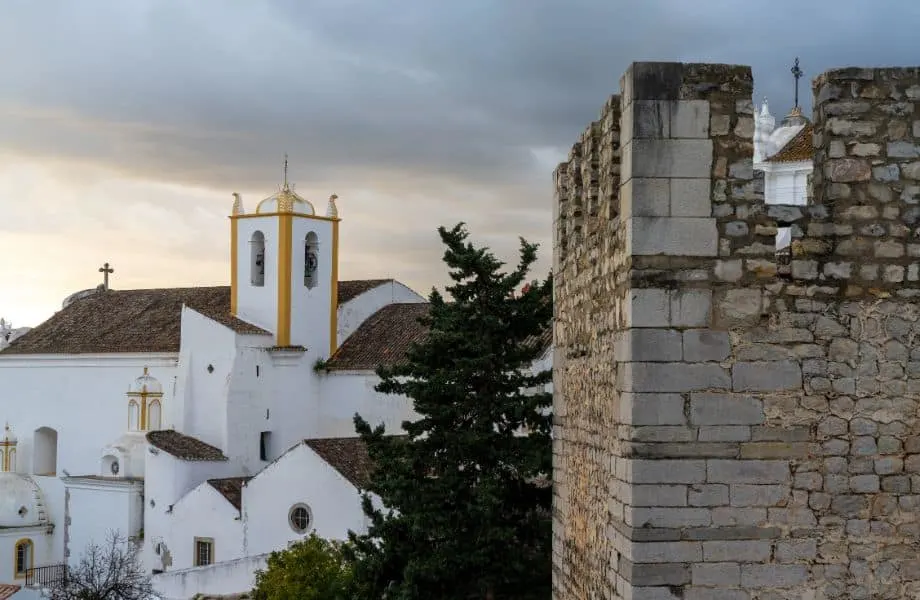 best things to see in Tavira, Stone castle tower fortification with large white church behind under an ominous grey cloudy sky at sunset