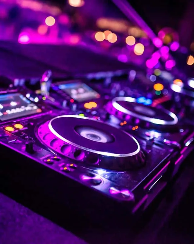 Close up shot of a DJ's mixing desk lit by pink and purple neon lights