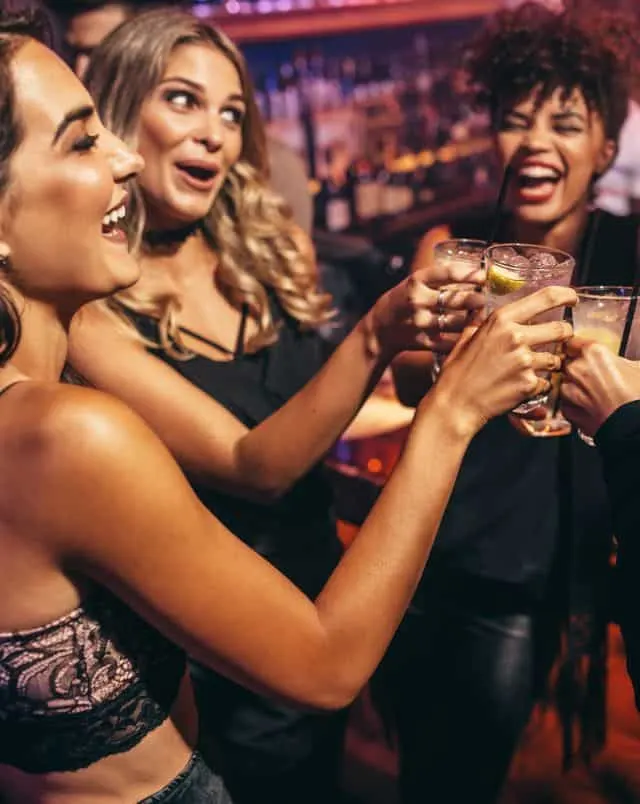 Several people in a bar smiling and putting their glasses of drinks together in celebration