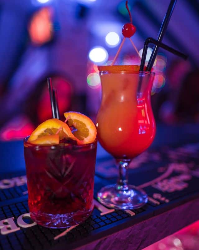 fun things to do in Milwaukee for couples at night, Close up shot of two cocktails with fruit and many straws sitting on a bar in a club