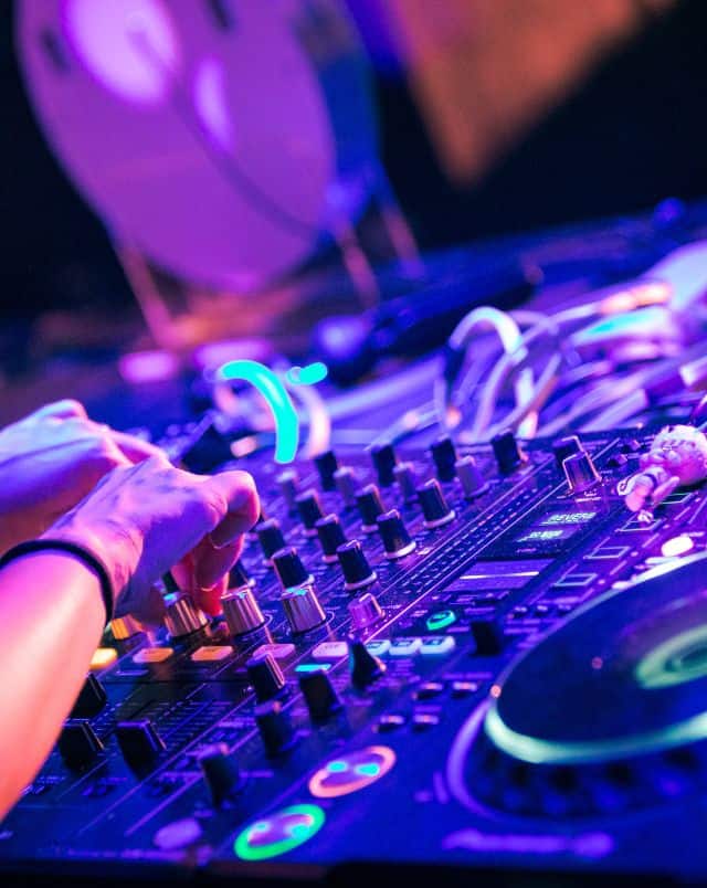 Close up shot of hands illuminated by neon lights working at a DJ's mixing desk in a club