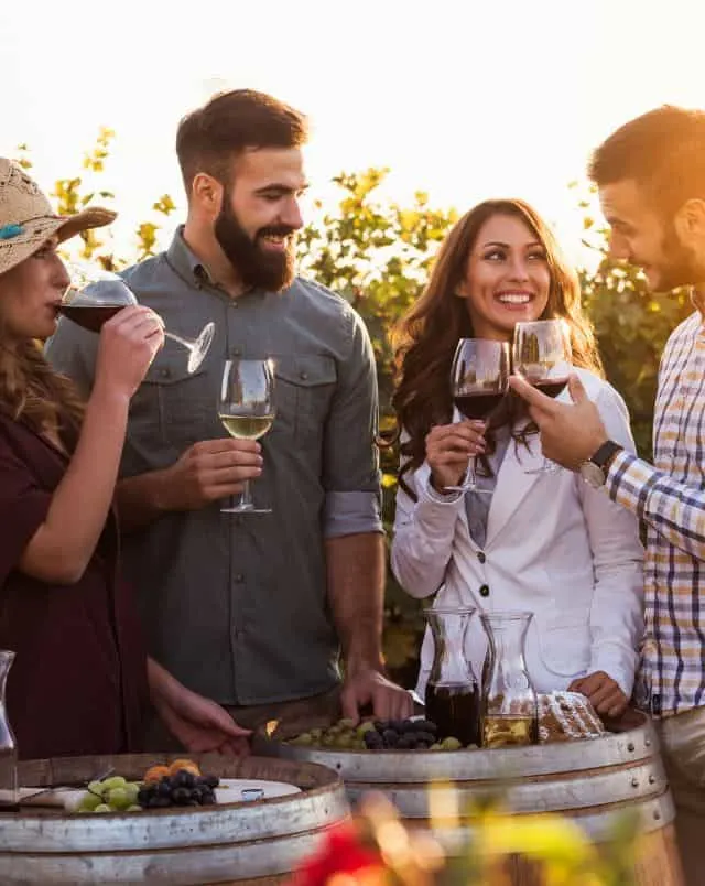 Southeastern Wisconsin wineries, Several people smiling and standing around some wooden barrels as they drink glasses of wine at sunset