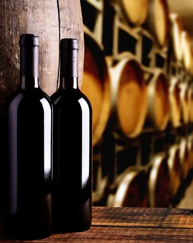 wineries of Southern Wisconsin, Close up shot of two bottles of wine standing on a wooden barrel with many other wooden barrels behind