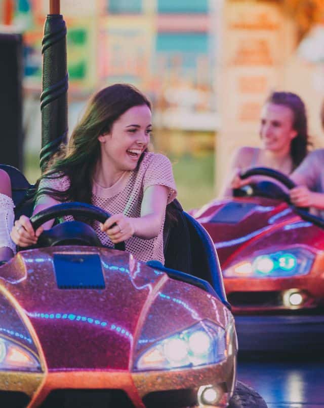 Why visit the Algarve in October, Close up shot of smiling person in vibrantly painted fairground bumper car with another smiling person in another bright bumper car behind