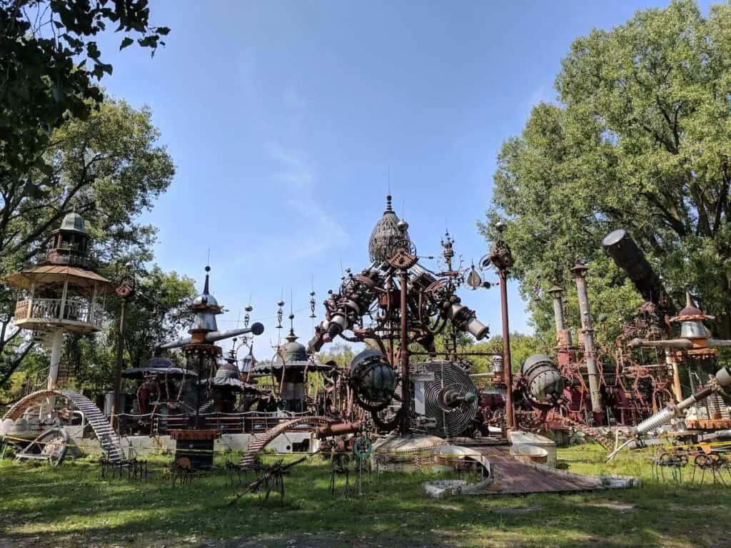weird Wisconsin roadside oddities, View of a large collection of metallic sculptures in a steampunk style sitting in a grassy area surrounded by green trees under a clear blue sky