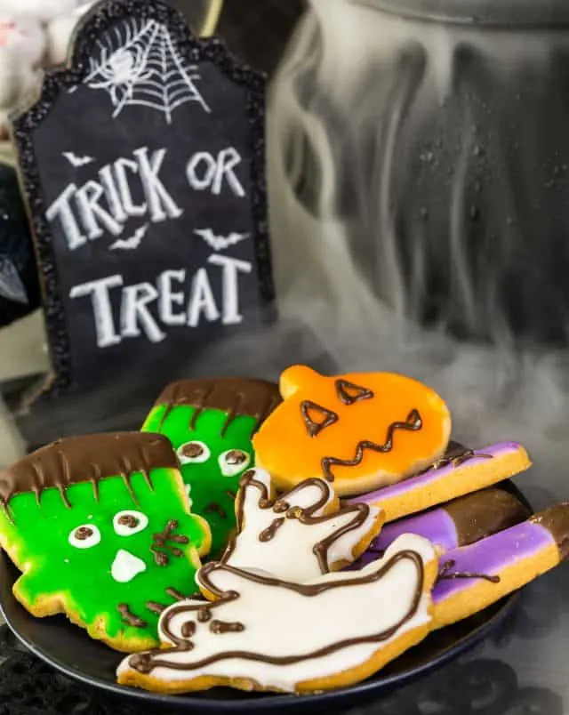 Close up shot of Halloween themed cookies in the shapes of spooky monsters under a sign shaped like a gravestone reading "Trick or Treat"