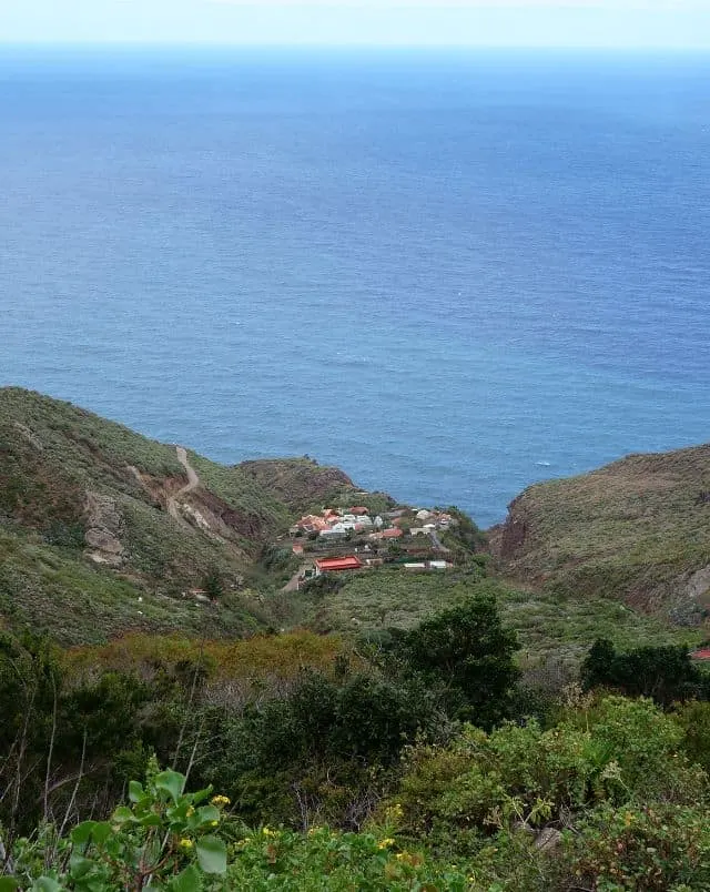 visit Tenerife in October, View of small valley with buildings visible in the distance surrounded by grassy hills next to the coast and the wide blue ocean stretching off to the horizon